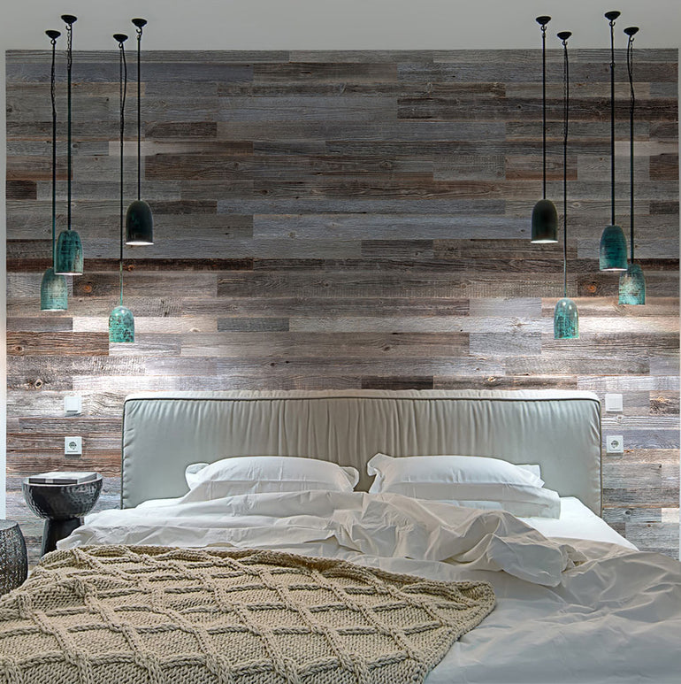 Une chambre à coucher moderne met en valeur un mur d'accent Parement Bois Anthracite de Wood & Wall Decor™, une grande tête de lit capitonnée, une literie blanche, une couverture en tricot beige et plusieurs lampes suspendues avec des nuances vertes et noires au-dessus du lit.