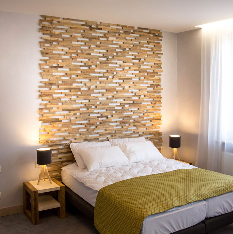 Une chambre à coucher moderne avec un lit habillé d'une literie blanche et d'une couverture verte, des tables de chevet avec des lampes, et un mur derrière le lit orné de Parement Bois Visio par Wood & Wall Decor™. La lumière naturelle filtre à travers un rideau transparent.